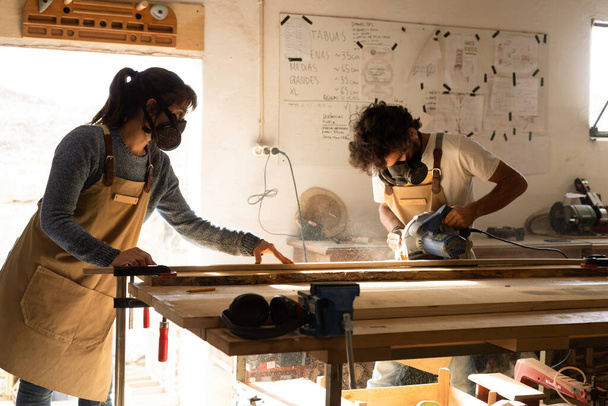 Jong koppel timmerman aan het werk en knutselen met hout in een atelier bouwmeubilair voor interieur. Jonge ondernemers die een klein bedrijf runnen in een timmerwerk. Zakenmensen. - Foto, afbeelding