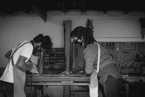 Fiatal asztalos pár, akik fával dolgoznak és dolgoznak egy műhelyben, bútorokat építenek belsőépítészeti célokra. Fiatal házaspár vállalkozók, akik kisvállalkozást működtetnek egy asztalosműhelyben. Üzletemberek. - Fotó, kép