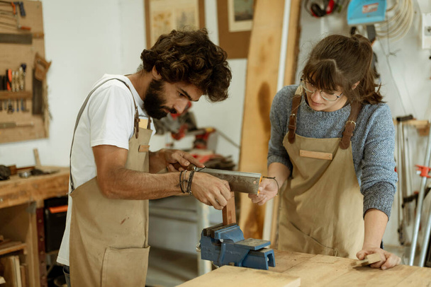 Jong koppel timmerman aan het werk en knutselen met hout in een atelier bouwmeubilair voor interieur. Jonge ondernemers die een klein bedrijf runnen in een timmerwerk. Zakenmensen. - Foto, afbeelding