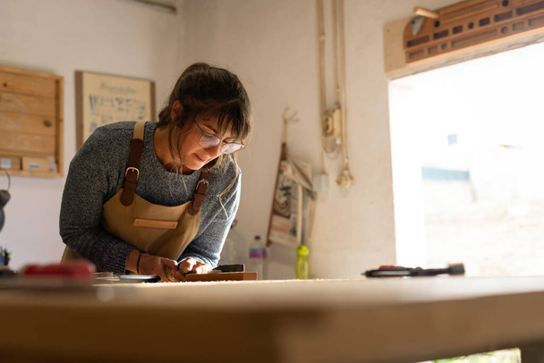 Una joven carpintera que trabaja como diseñadora de madera en un pequeño taller de carpintería. Joven mujer de negocios artesanal un pedazo de madera y el diseño de nuevos muebles de la casa. Empresarios concepto estilo de vida - Foto, Imagen