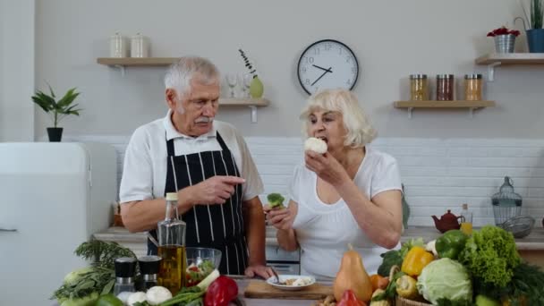 Seniorenpaar in der Küche. Ältere Großmutter und Großvater essen rohen Brokkoli und Blumenkohl - Filmmaterial, Video