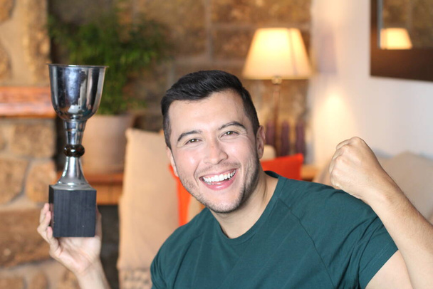 自宅でチャンピオンカップを持っているハンサムな若い男のクローズアップ肖像 - 写真・画像