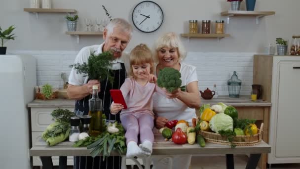 blogger ragazza facendo selfie al telefono con anziani nonni coppia in cucina con verdure - Filmati, video