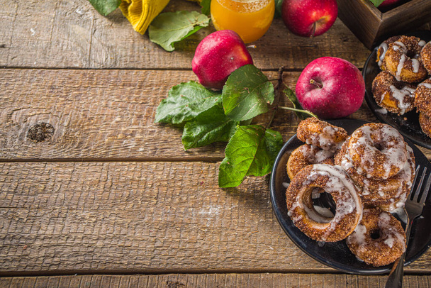 Jesienny słodki przepis na deser. Domowej roboty pączki jabłkowe. Pieczone pączki z cukrem, polewą cynamonową i polewą z cukru białego, na drewnianym tle ze świeżymi jabłkami  - Zdjęcie, obraz