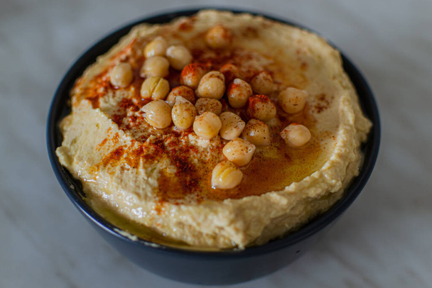 Homemade creamy hummus with chickpeas and red spices in dark plate in vegetarian kitchen. Top view - Fotó, kép