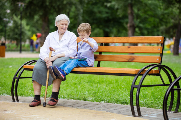 Молодий хлопчик і його бабуся використовують планшет в парку
 - Фото, зображення