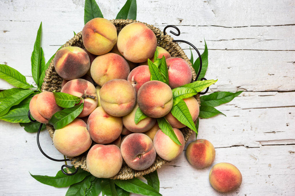 Ripe red peaches in a basket on a rustic white table, top view. Healthy organic fruit. - Photo, Image