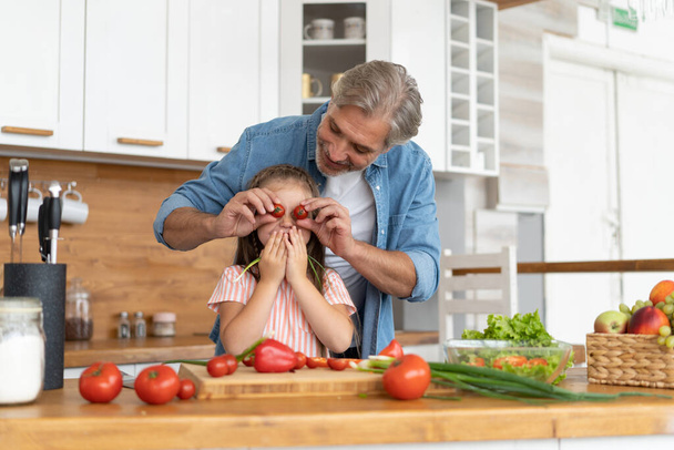Cute little girl and her handsome dad are having fun while cooking in kitchen at home. - Foto, Bild