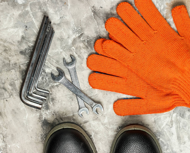 Schraubenschlüssel, Stiefel und Handschuhe auf grauem Betongrund. Arbeitswerkzeug. Ansicht von oben - Foto, Bild