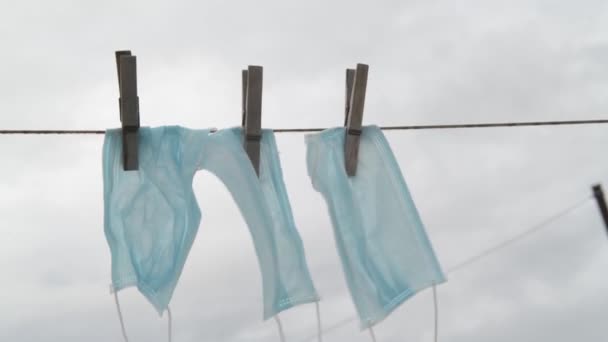 Medizinische Schutzmasken wiegen auf einem Seil zum Trocknen nach dem Waschen vor einem grauen Herbsthimmel. zur Wiederverwendung während Covid-19. Coronavirus zerstört Wirtschaft und Gesundheit - Filmmaterial, Video