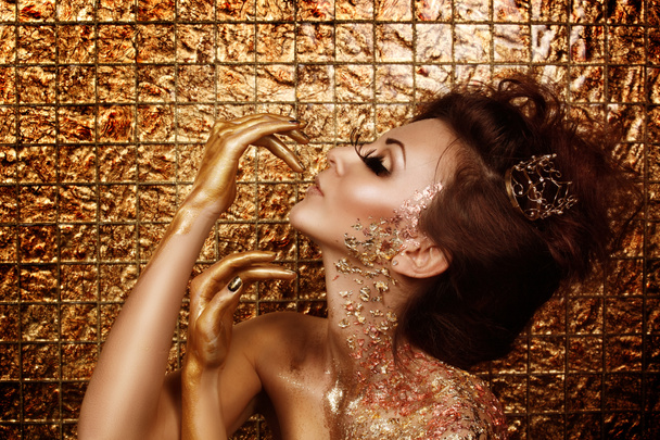attraktive süchtig heiße Brünette mit schönen goldenen Make-up und goldenen Karamell bemalten Händen posiert vor abstrakten goldenen Hintergrund - Foto, Bild