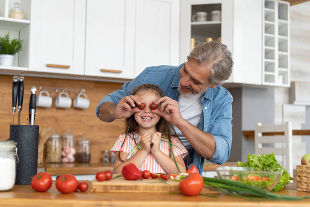 Cute little girl and her handsome dad are having fun while cooking in kitchen at home. - Foto, imagen
