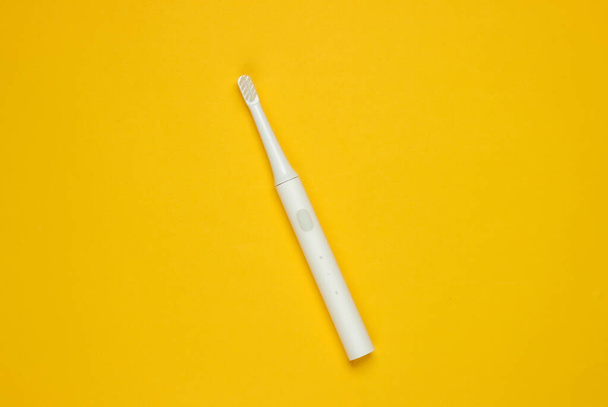 Сучасна електрична зубна щітка на жовтому тлі. Концепція стоматологічної допомоги. Вид зверху. Мінімалізм
 - Фото, зображення