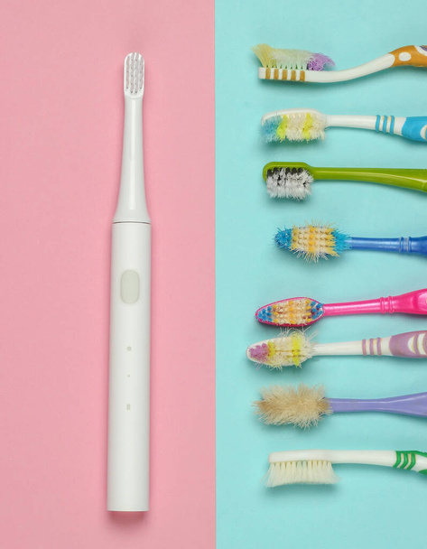 Moderní elektrický zubní kartáček a staré použité zubní kartáčky na růžovém modrém pastelovém pozadí. Horní pohled - Fotografie, Obrázek