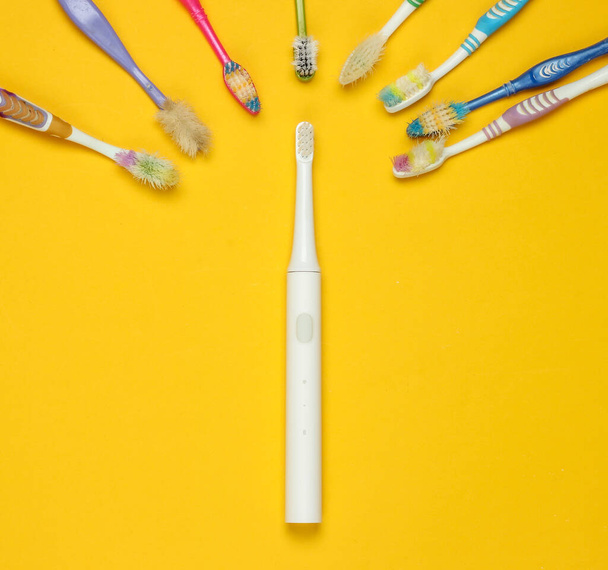 Modern elektromos fogkefe és régi használt fogkefék sárga háttérrel. Felülnézet - Fotó, kép