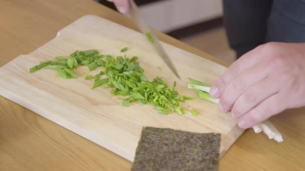 Cook cuts green onions on wooden chopping board in home kitchen close up - Footage, Video