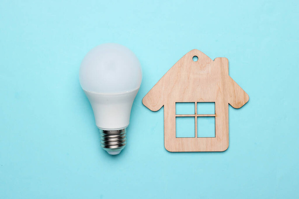 Save energy concept. Eco house concept. Mini house and energy-saving light bulb on a blue background - Foto, imagen