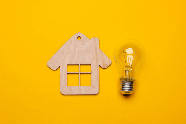 Save energy concept. Mini house, incandescent light bulb on yellow background. Top view - Foto, imagen