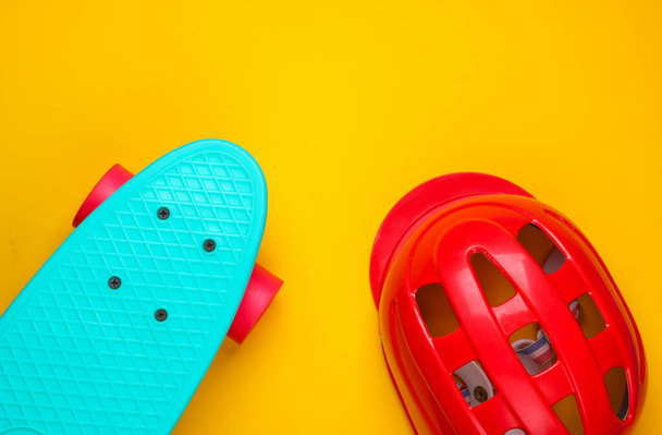 Cruiser board and safety helmet on a yellow background. Protective equipment for sports. Childhood. Top view - Photo, Image