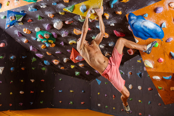 Joven hombre bouldering en interior escalada gimnasio, tratando de resolver desafiante problema - Foto, imagen