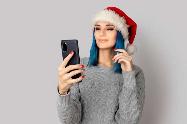 Hermosa mujer joven feliz en sombrero de santa tomar selfie sobre fondo gris. Navidad año nuevo concepto de celebración - Foto, Imagen