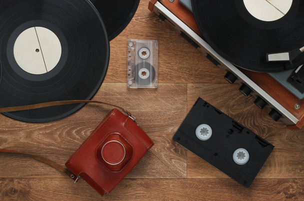 Old vinyl record player, video cassettes, audio cassette, old-fashioned film camera on the floor. Retro media 80s. Top view - Photo, image