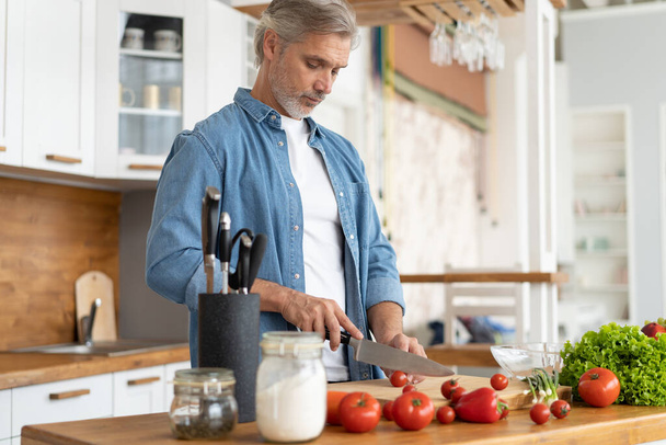 Grey-haired Mature handsome man preparing delicious and healthy food in the home kitchen. - Foto, afbeelding