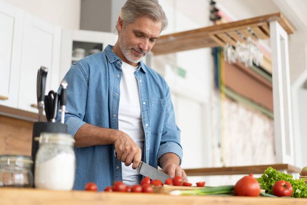 Grey-haired Mature handsome man preparing delicious and healthy food in the home kitchen. - Valokuva, kuva