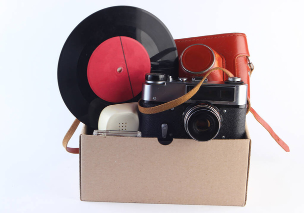 Kartonschachtel mit Retro-Filmkamera, Gamepad, Schallplatte, Telefonröhre auf weißem Hintergrund. Antiquitäten, Müll - Foto, Bild
