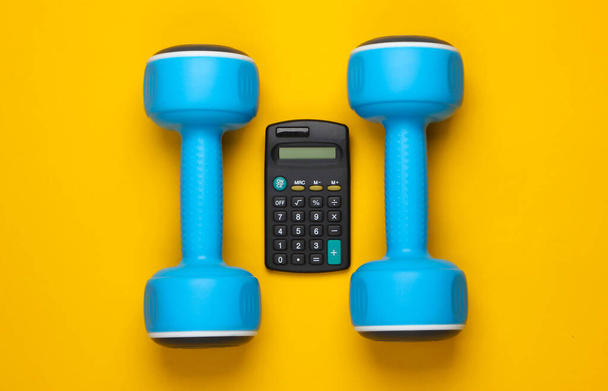 Fitness, concept sportif. Calorie Counting. Calculatrice et haltère sur fond jaune. Vue du dessus - Photo, image