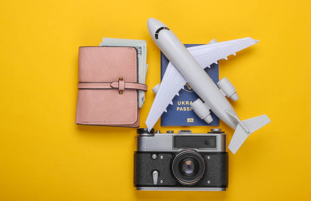 Flache Reisekomposition auf gelbem Hintergrund. Flugzeugfigur, Reisepass, Geldbörse mit Dollars, Kamera. Erholung, Urlaub und Tourismus, Minimalismus-Konzept. Ansicht von oben - Foto, Bild