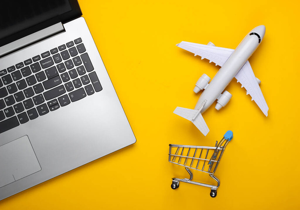 Lapos kompozíció. Légi szállítás. Online vásárlás. Laptop, bevásárlókocsi figurája, sárga hátterű repülőgép. Felülnézet - Fotó, kép
