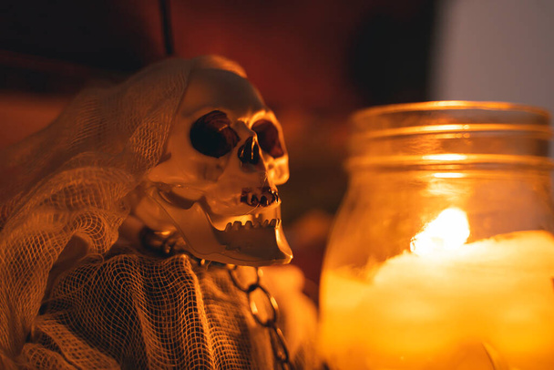 a decorative human skull hangs on chains next to a burning candle - Foto, Bild