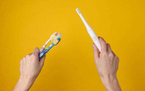 Female hand holds a modern electro-toothbrush with charger on  yellow background. Top view - 写真・画像