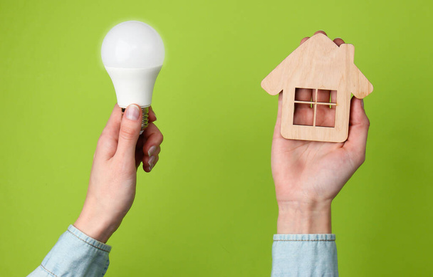 Eco, economize energia conceito. As mãos femininas mantêm a figura de casa e a lâmpada em um contexto verde. Vista superior - Foto, Imagem