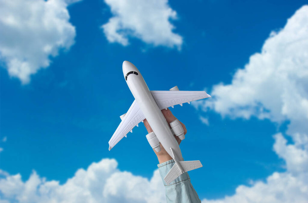 La mano femenina sostiene un avión de juguete contra el cielo azul con nubes blancas. Concepto de viaje - Foto, imagen