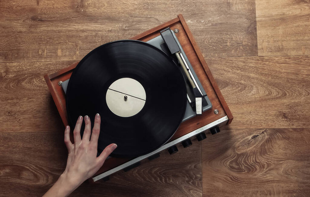Weibliche Hände stellen einen Retro-Plattenspieler auf einem Holzboden auf. Musikliebhaber, 70er Jahre, Nostalgie, Draufsicht - Foto, Bild