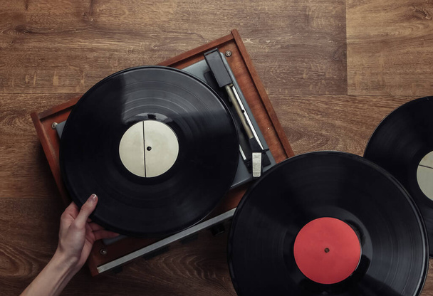 Ženské ruce vyzvednout vinylovou desku pro vinylového hráče na dřevěné podlaze. Milovník hudby, 70. léta, pohled shora, nostalgie - Fotografie, Obrázek