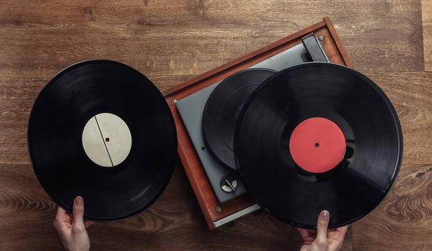 Female hands pick up vinyl record for vinyl player on a wooden floor. Music lover, 70s, top view, nostalgia - Photo, Image