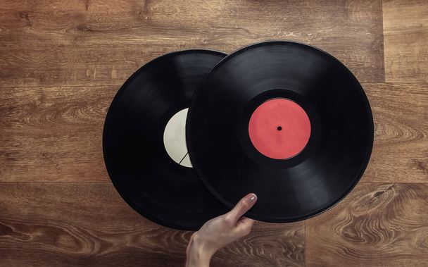Female hand holds two vinyl records on a wooden floor. Top view - Photo, Image