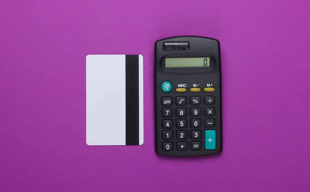 Kalkulator i karta bankowa na fioletowym tle. Widok z góry - Zdjęcie, obraz