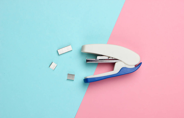 Engrapadora con clips de papel sobre un fondo pastel de color rosa azulado. Minimalismo. Vista superior - Foto, Imagen