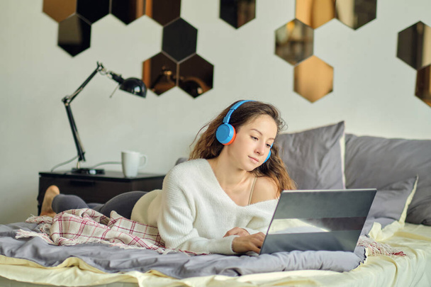 Young beautiful woman wearing headset while using laptop in bed - Photo, Image