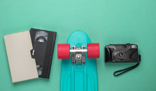 Amusant. Plat de la jeunesse. Cruiser board avec une caméra rétro, cassette vidéo sur fond bleu pastel. Rétro années 80. Vue du dessus - Photo, image