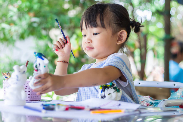 Portraitbild eines 2 bis 3 Jahre alten Babys. Glückliches asiatisches Kindermädchen lächelnd und mit Stoffmaske. Sie zeigt mit dem Finger auf den Spielplatz. Soziale Distanz. Lern- und Aktiv-Konzept für Kinder. - Foto, Bild
