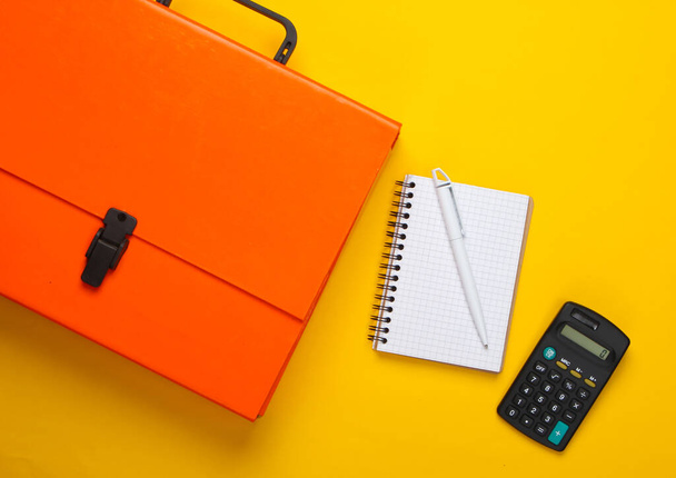 黄色の背景にオレンジの紙ケース、ノートブック、計算機。トップ表示 - 写真・画像