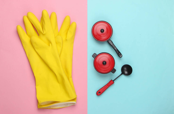Flat lay composition of cleaning gloves, toy kitchen tools and utensils on blue pink pastel background. Top view - Photo, Image