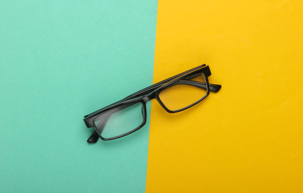 Classic eyeglasses on a yellow-blue background. Top view. Minimalism - Фото, изображение