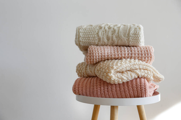 Stack of clean freshly laundered, neatly folded women's clothes on wooden table. Pile of shirts, dresses and sweaters on the table, white wall background. Copy space, close up, top view. - Foto, imagen