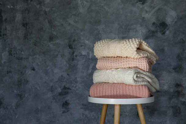 Stack of clean freshly laundered, neatly folded women's clothes on small table. Pile of shirts, dresses and sweaters on the table, concrete wall background. Copy space, close up, top view. - 写真・画像